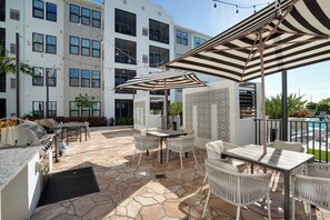 A patio with stone flooring, outdoor furniture, a grill, and a pool in the background. - 2BR Coastal Condo in Bradenton | 3 Mi to IMG (Bradenton)