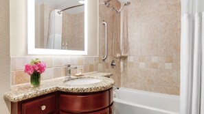 Ein Badezimmer mit Granitwaschtisch, einem Spiegel, einer Dusche mit Handbrause und einer Badewanne.