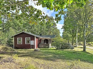 A small, single-story wooden cabin with a porch, surrounded by trees and grass. - Tallstugan by Interhome (Kisa)