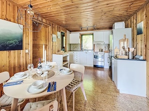 A wooden interior with a dining area, kitchen, and a dining table set for four. - Tallstugan by Interhome (Kisa)