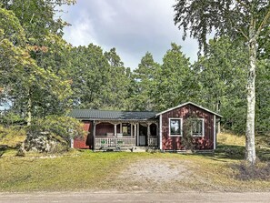 A small, single-story wooden cabin with a porch, surrounded by trees. - Tallstugan by Interhome (Kisa)