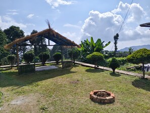 A well-maintained garden with a thatched-roof gazebo, neatly trimmed bushes, and a brick fire pit.