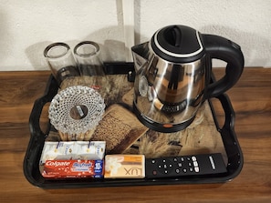 A tray with a coffee maker, two glasses, a packet of Colgate toothpaste, a box of Maxfresh, and a remote control. - Comfort Castle Homestay (Kalimpong)