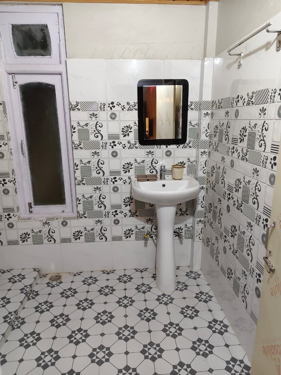 Ein Badezimmer mit einem weißen Waschbecken, einem Spiegel und einem Musterfliesenbelag an Wänden und Boden.