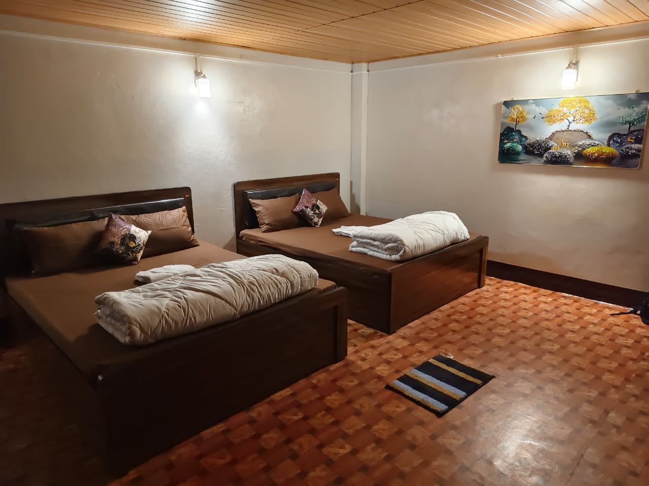 Una habitación con dos camas, piso de madera y un cuadro en la pared.