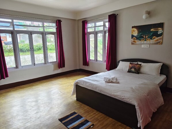A hotel room with a large bed, two windows with curtains, a painting on the wall, and a wooden floor.
