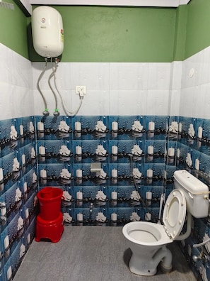 Un baño con inodoro, un cubo rojo y un calentador de agua en la pared.