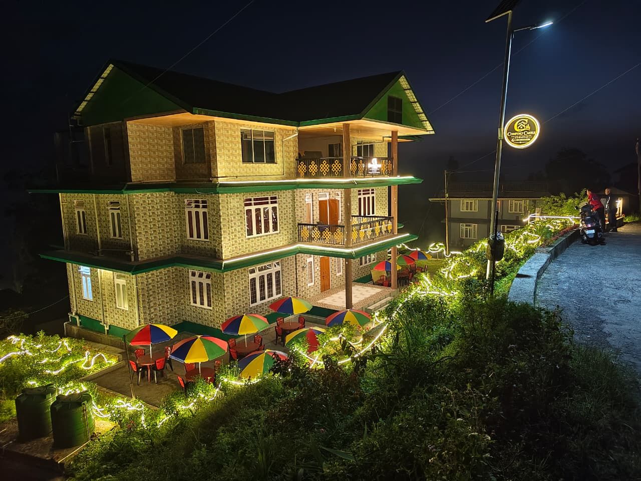 A two-story building with a balcony, outdoor seating with umbrellas, and a well-lit entrance.