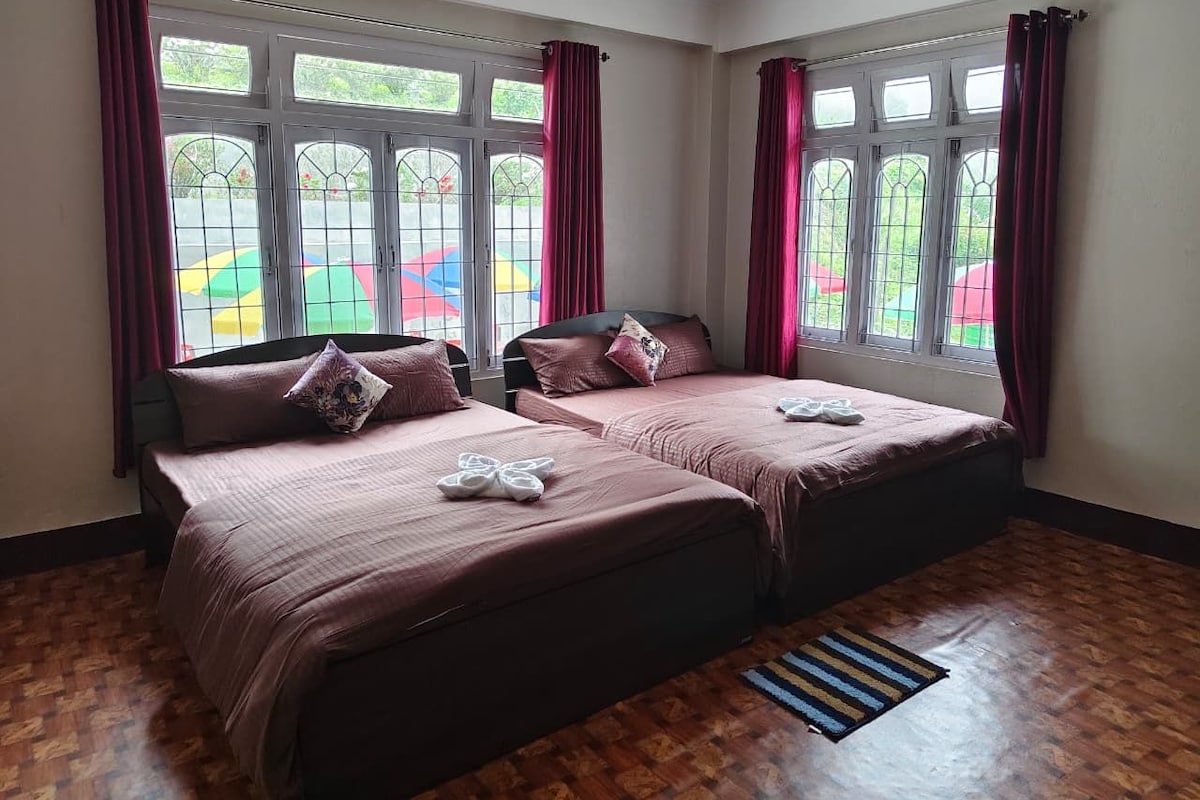 Habitación con dos camas, piso de madera y ventanas con cortinas.