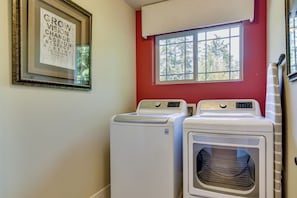 A laundry room with two front-loading washing machines, a framed inspirational quote on the wall, and a window with a view of trees. - 3BR Beaverton Home, Extended Retreat! (Beaverton)
