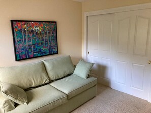 Une pièce avec un canapé beige, un tableau abstrait aux couleurs vives et une porte blanche.