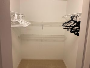 Un dressing avec des cintres blancs et noirs, une étagère blanche et un tapis beige.