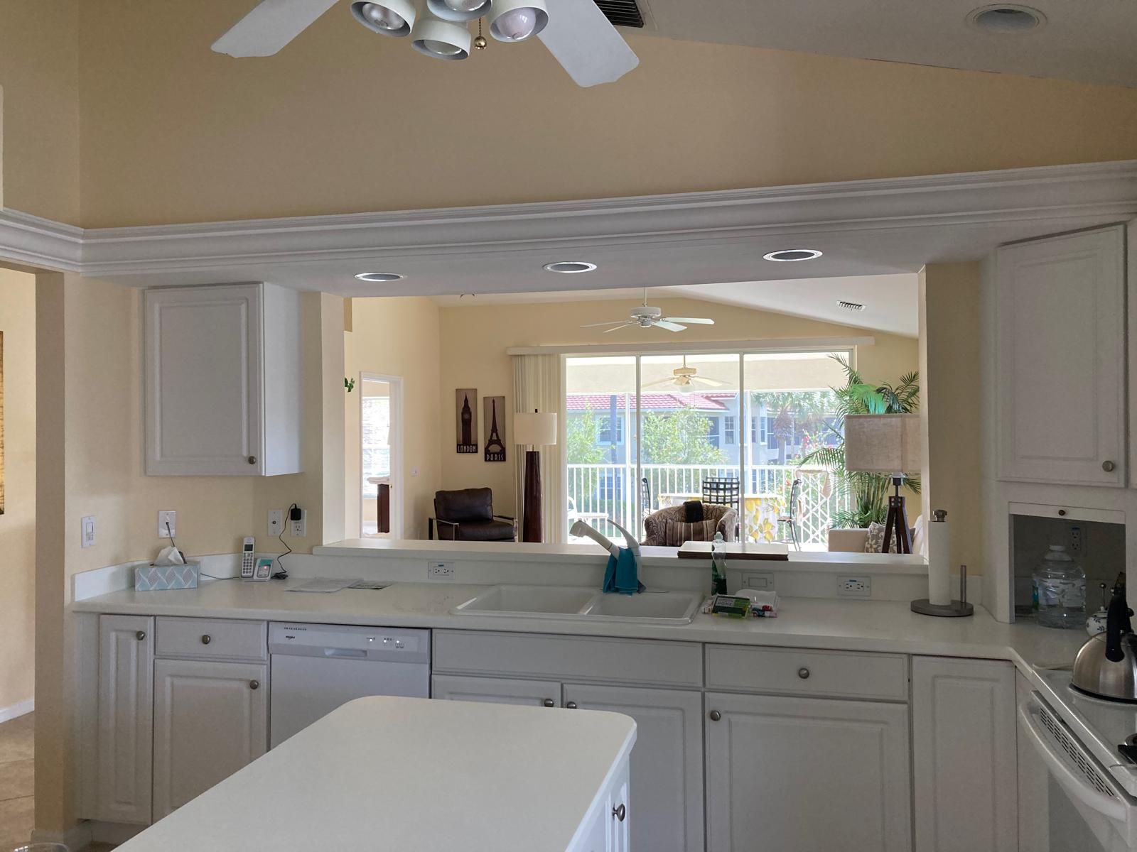 A kitchen with white cabinets, a countertop, a ceiling fan, and a view of the outside.