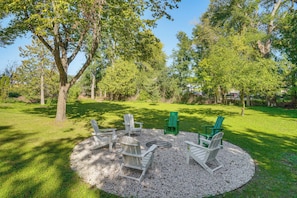 A circular seating area with chairs and a fire pit surrounded by gravel, set in a grassy outdoor space with trees. - Great for Families! Egg Harbor Gem w/ Beach Access (Egg Harbor)