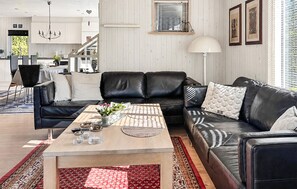 Una sala de estar moderna con un sofá de cuero negro, una mesa de centro de madera y un tapete rojo estampado.