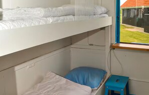 Habitación con literas, una ventana, un taburete pequeño y una puerta visible.