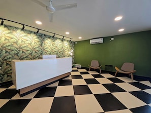 A reception area with a checkered floor, a reception desk, two chairs, a ceiling fan, and an air conditioning unit. - Manzl Collective Peepal  (Tada)