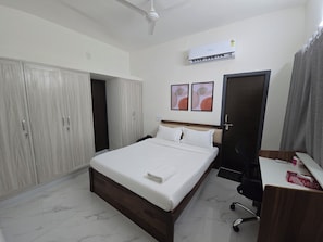 A hotel room with a bed, wardrobe, desk, and air conditioning unit. - Manzl Collective Peepal  (Tada)
