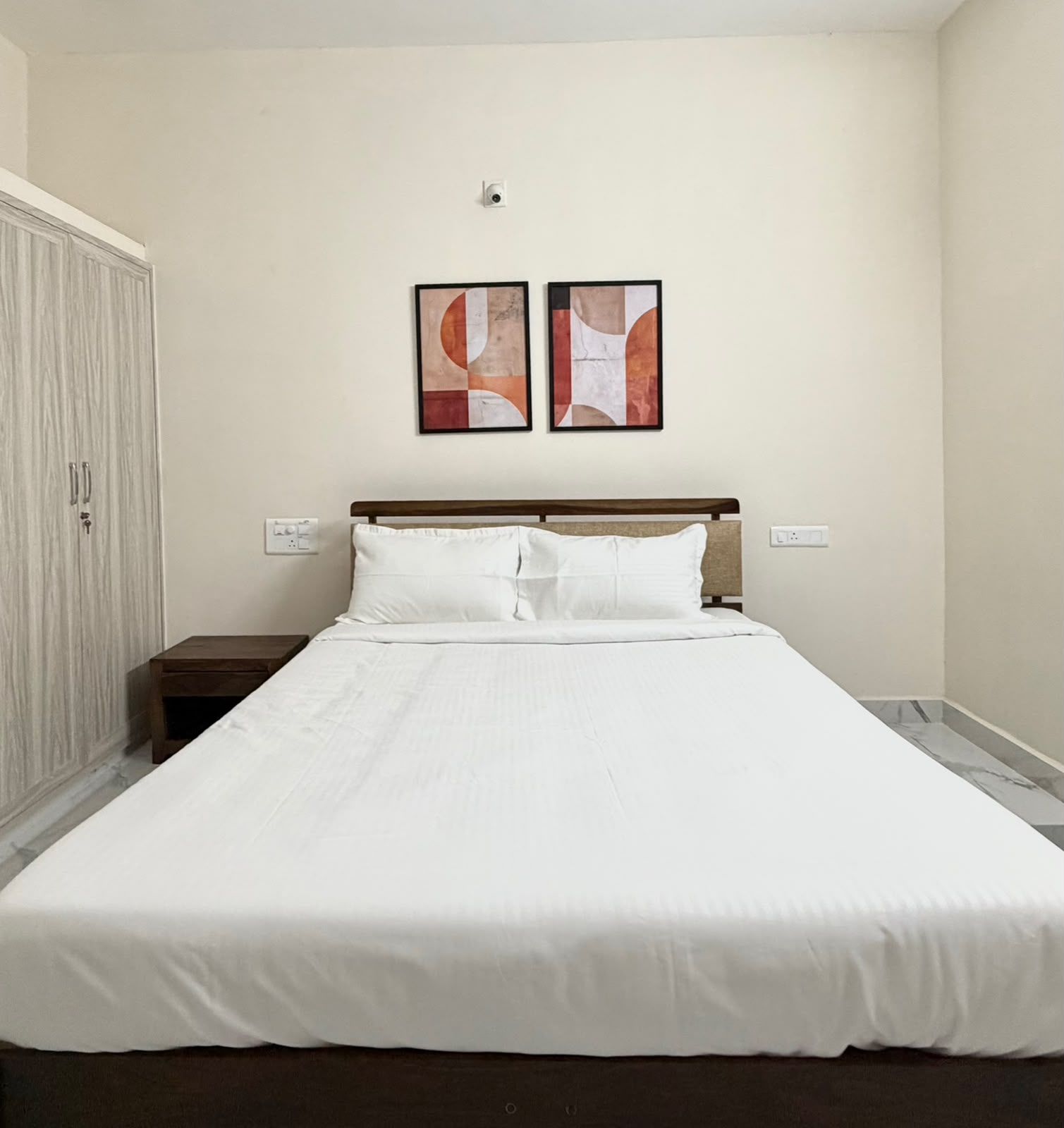 Un dormitorio con una cama, una mesita de noche, un armario y dos cuadros abstractos en la pared.