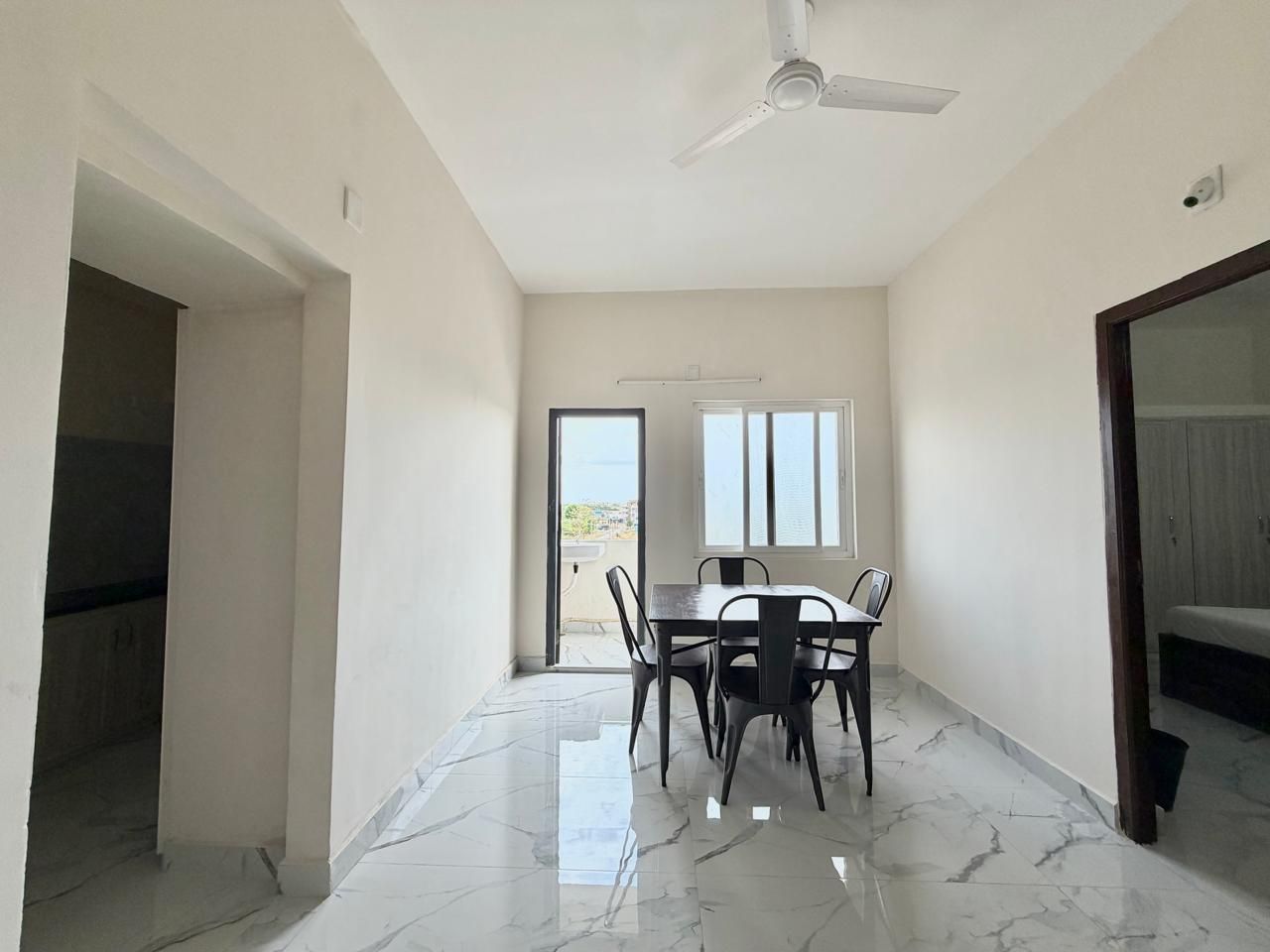 A room with a dining table and chairs, a ceiling fan, and a view through a door.