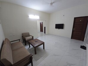 A living room with a sofa, armchair, coffee table, and a flat-screen TV mounted on the wall.