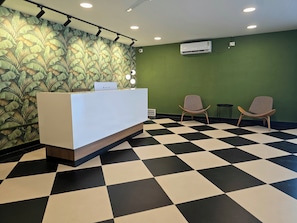 Una zona d'entrada amb un paviment a escacs, una taula de recepció, dues cadires i una paret amb un disseny de fulles.