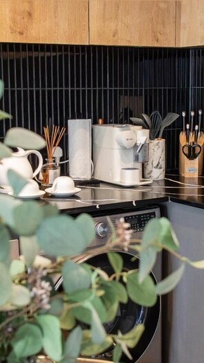 Et køkken med vaskemaskine, kaffemaskine og diverse køkkenredskaber.