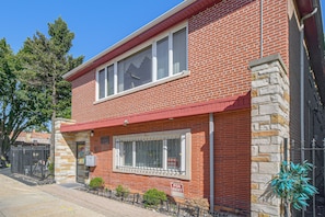 A two-story brick building with a red roof, a 'For Rent' sign, and a small garden area with a fence. - Chicago South Side Studio w/ Gated Parking (Chicago)