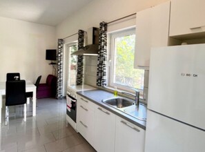 A compact kitchen with white cabinets, a Bosch refrigerator, a window with a view, and a dining area with a chair and table. - Paradise Apartments-studio Apartman With sea View and Terrace 2 (Jelsa)