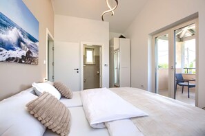 A modern bedroom with a large bed, a painting of a wave, and a balcony with a chair. - Terracotta Hillside Hideaway Vranje (Vizinada)