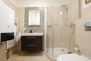 Ein modernes Badezimmer mit Duschkabine aus Glas, einem weißen Waschbecken und einem dunkelholzfarbenen Waschtisch.