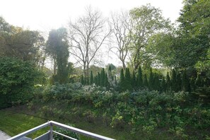 Um jardim com diversas árvores e arbustos, cerca de madeira e grades de metal.