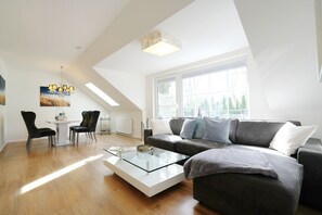 A modern living room with a glass coffee table, a grey sofa, and a dining area with a white table and chairs. - Niendorf Residential Park, Apartment 7 - Niendorf Residential Park 13 (Timmendorfer Strand)