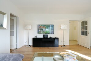 A modern living room with a black entertainment unit, a flat-screen TV, and two floor lamps. - Niendorf Residential Park, Apartment 7 - Niendorf Residential Park 13 (Timmendorfer Strand)