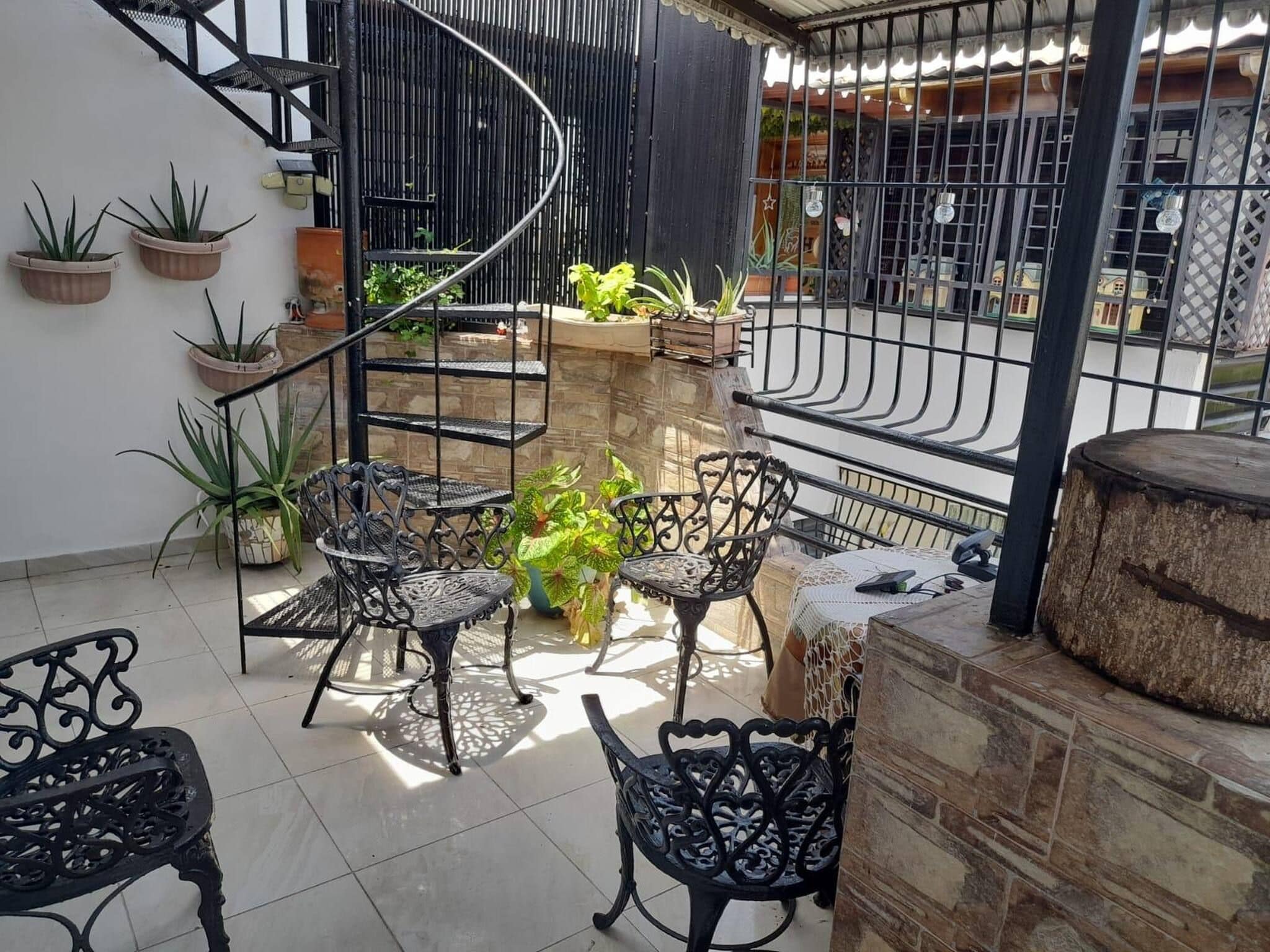 A sunlit outdoor patio with a spiral staircase, potted plants, and ornate metal furniture.