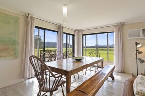Ein Essbereich mit Holztisch, Stühlen und einer Bank. Große Fenster bieten Blick auf eine grüne Landschaft.