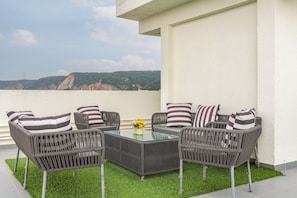 A terrace with wicker furniture, a glass table, and a view of a mountain. - ELIVAAS Signature Aura Sky 3 BHK Apt (Jaipur)