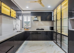 A modern kitchen with black cabinets, a marble floor, and a window with a view. - ELIVAAS Signature Aura Sky 3 BHK Apt (Jaipur)