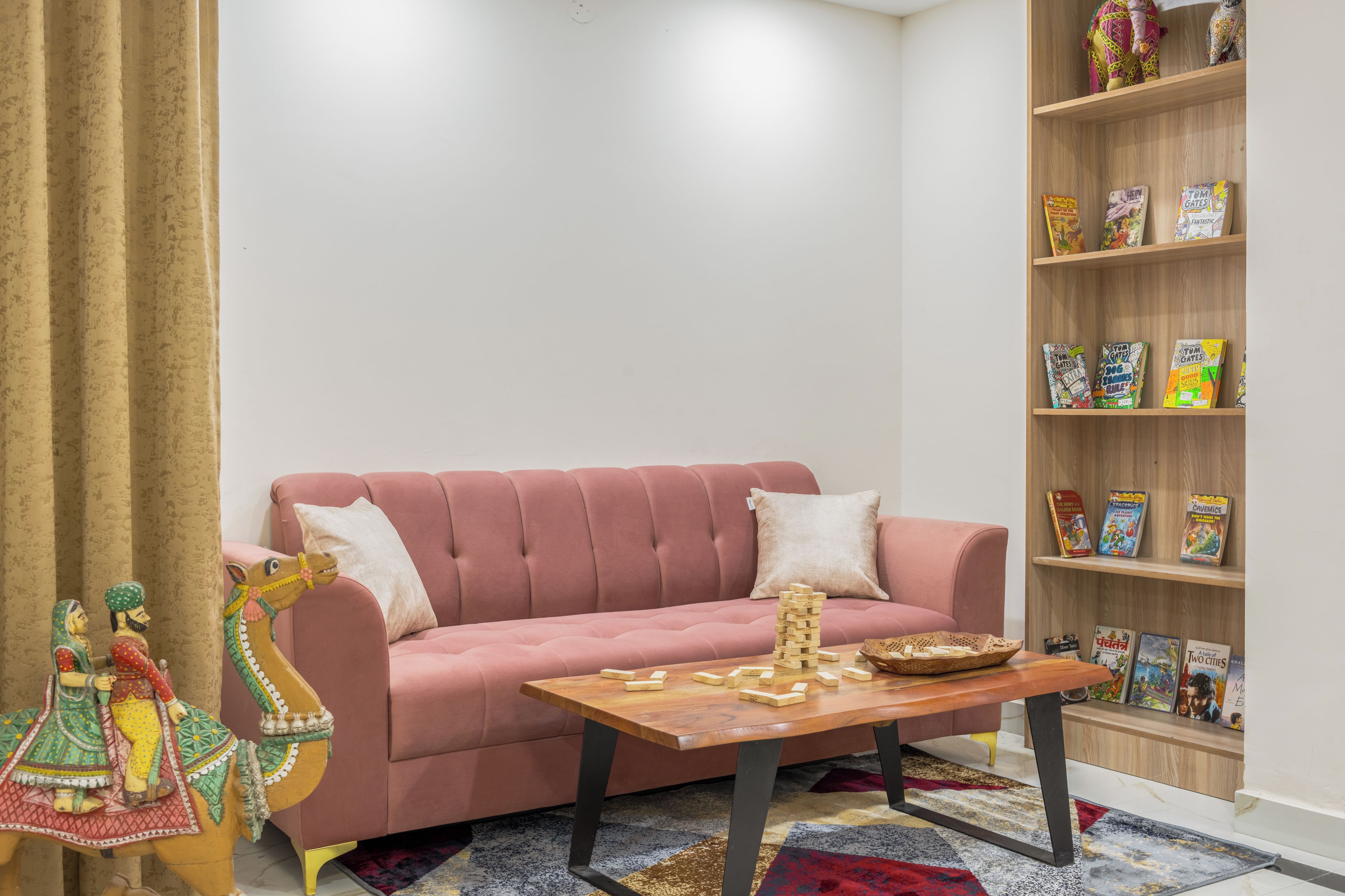 Una sala de estar con un sofá rosa, una mesa de centro, una estantería llena de libros infantiles y una estatua decorativa de un elefante.