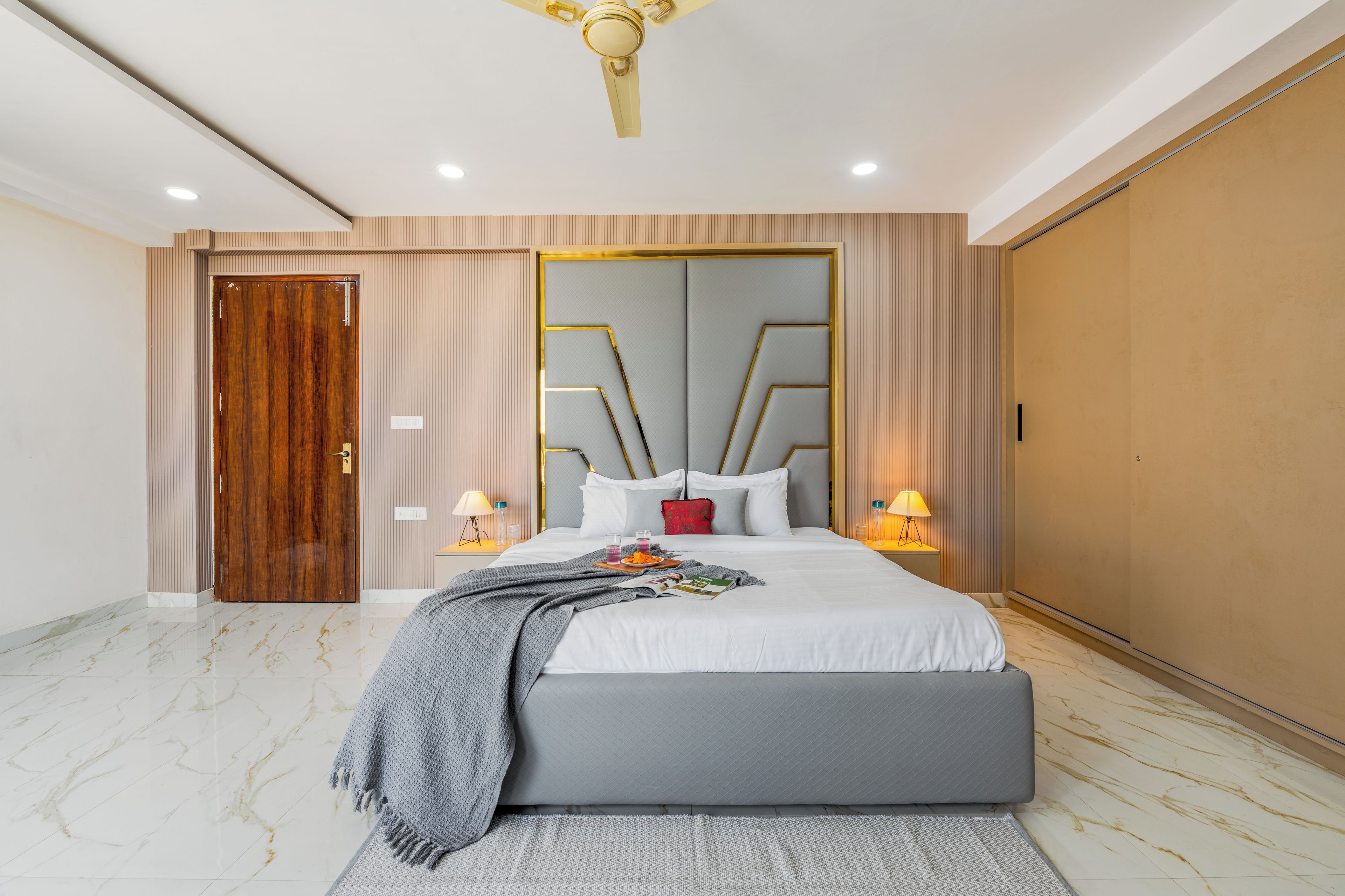 A modern bedroom with a large bed, bedside lamps, a wooden door, and a ceiling fan.