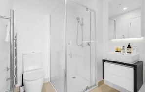Une salle de bain moderne avec une douche à parois de verre, un lavabo blanc agrémenté d’articles de toilette et un miroir au-dessus du lavabo.