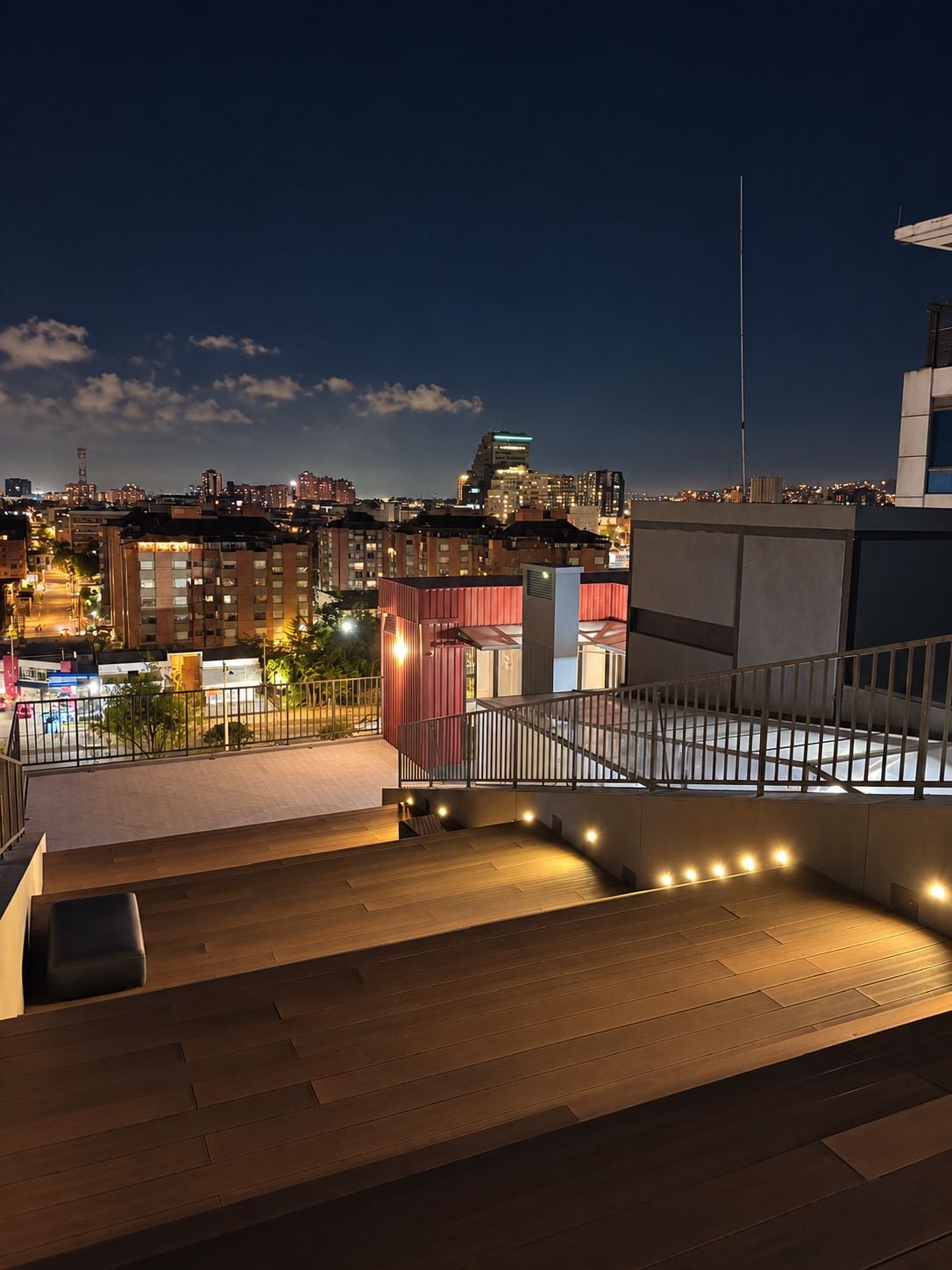 A rooftop terrace with a view of a city skyline at night.
