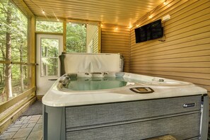Een bubbelbad in een kamer met houten wanden en een raam met uitzicht op een bos.