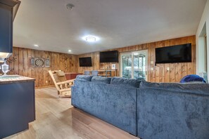 Ein Wohnzimmer mit Holzboden, einem blauen Sofa, einem Holzstuhl und einem an der Wand befestigten Flachbildfernseher.