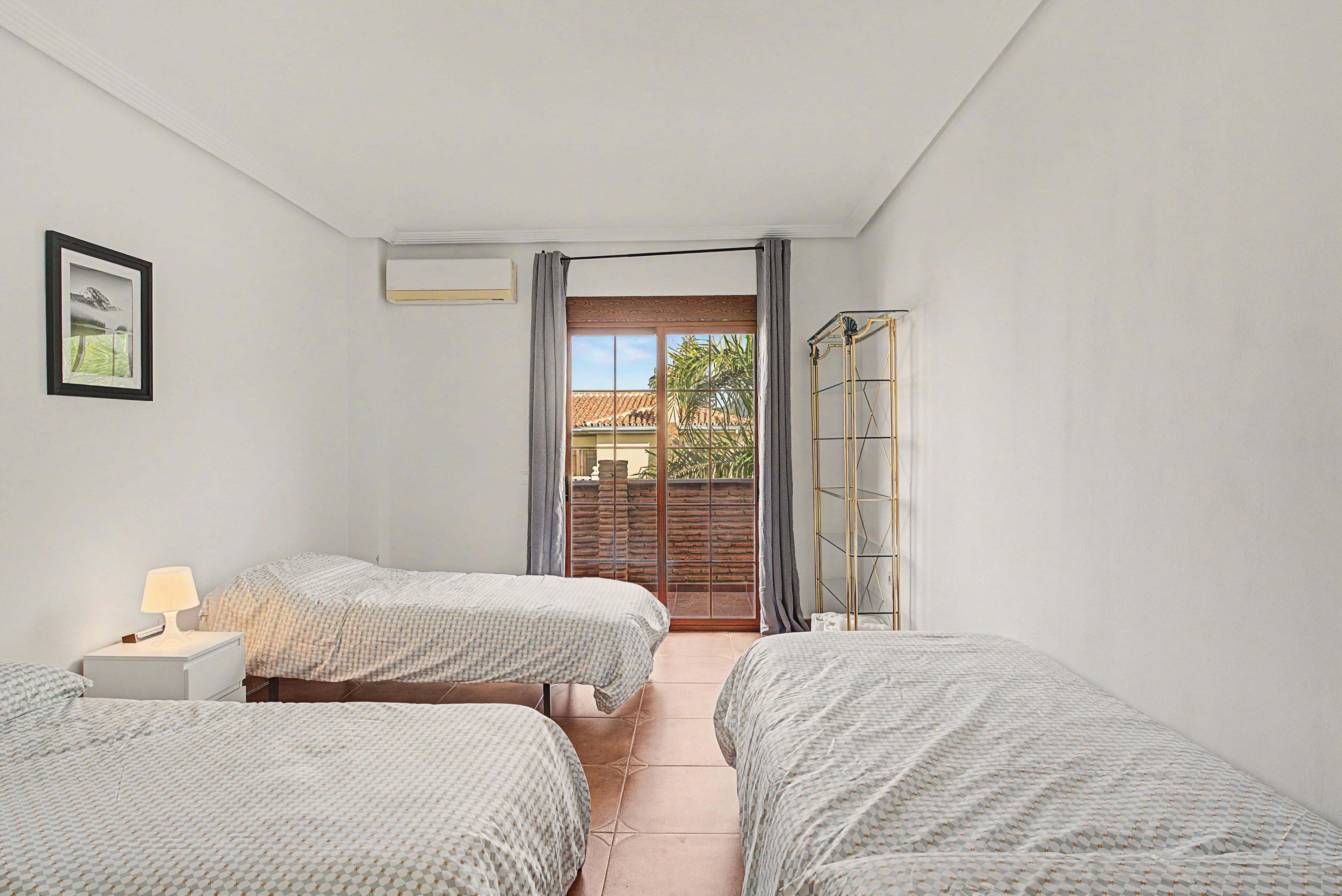 Un dormitorio con dos camas, una mesita de noche, una lámpara, un cuadro enmarcado y vistas al exterior.