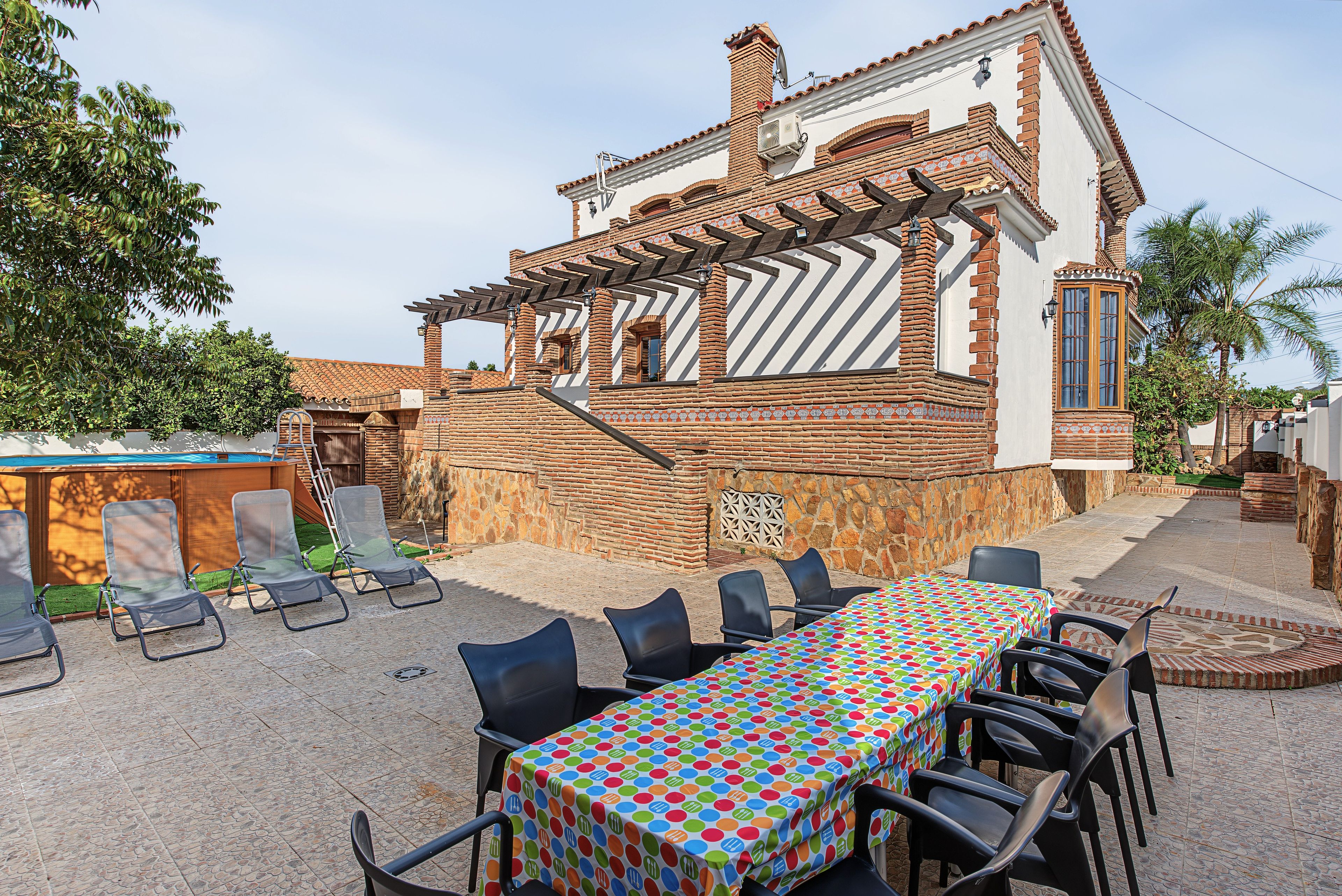 Een terras met een tafel en stoelen, een zwembad en een huis met bakstenen muren en een betegeld dak.