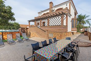 Un espace patio avec une table et des chaises, une piscine et une maison en briques avec un toit en tuiles.