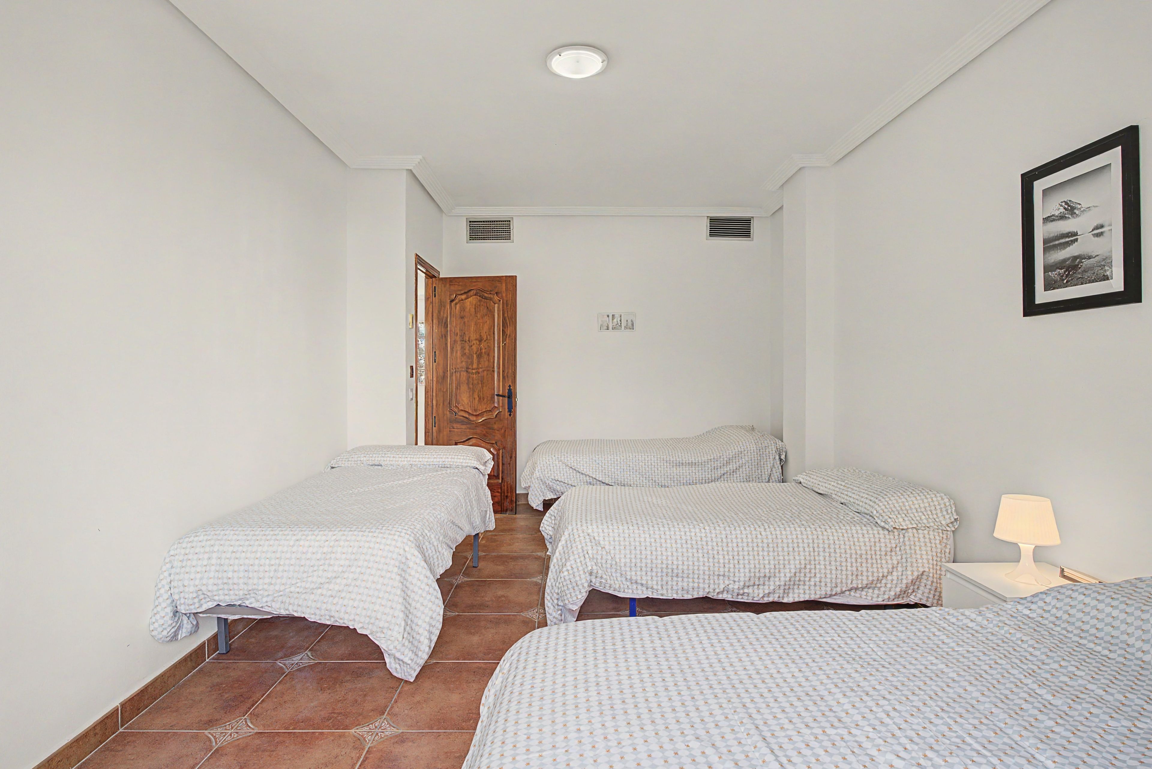 A hotel room with two single beds, a wooden door, a small window, and a framed picture on the wall.