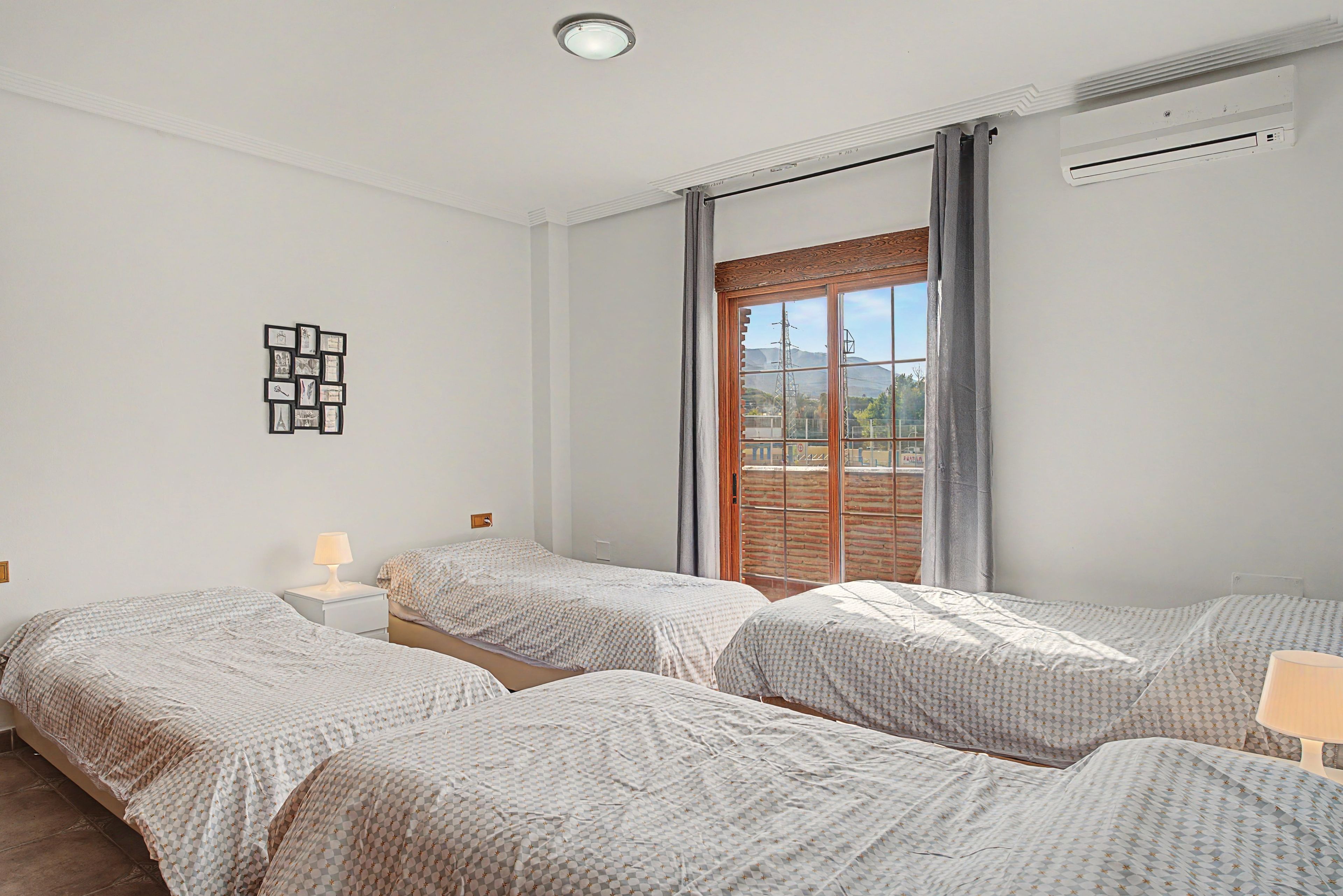 Habitación de hotel con dos camas, una mesita de noche, un cuadro en la pared y un ventanal con cortinas.