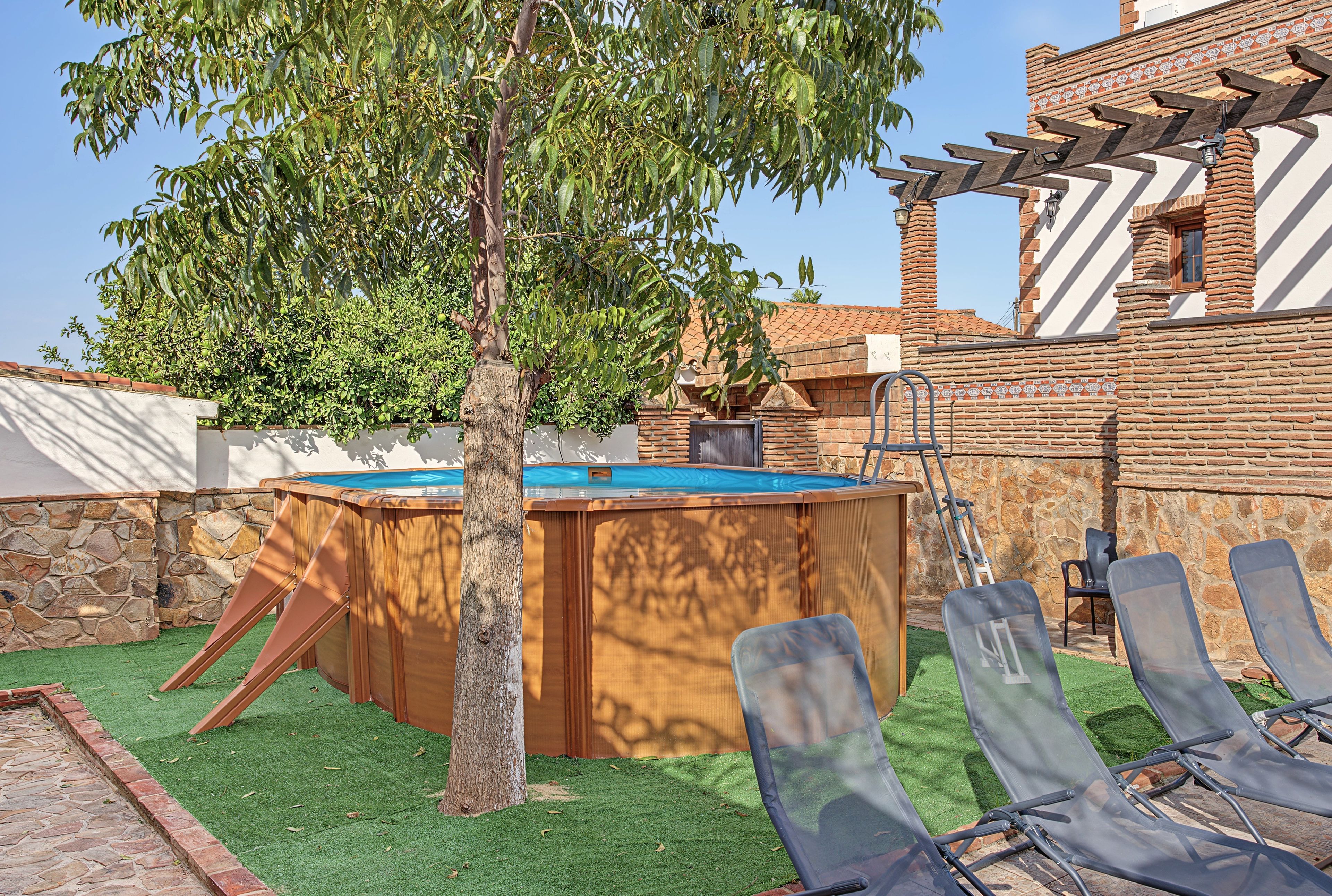 Ein Poolbereich mit Holzterrasse, Liegestühlen und einer Pergola.